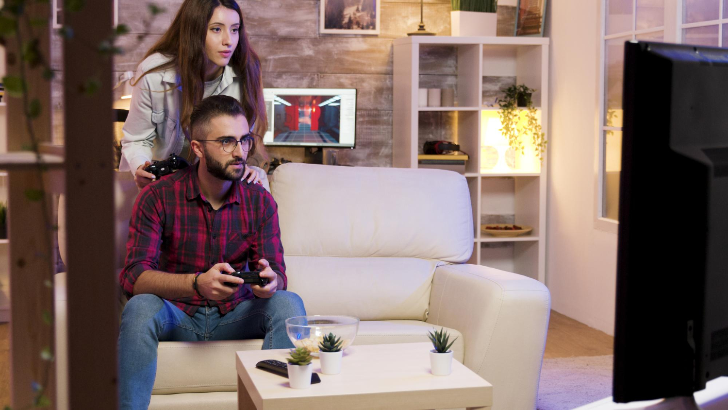 A guy is sitting on a couch with a joystick and playing a console.
